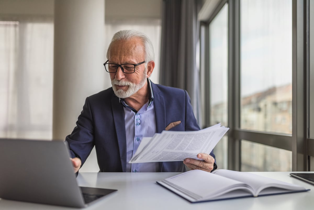 A person at a laptop holding papers.