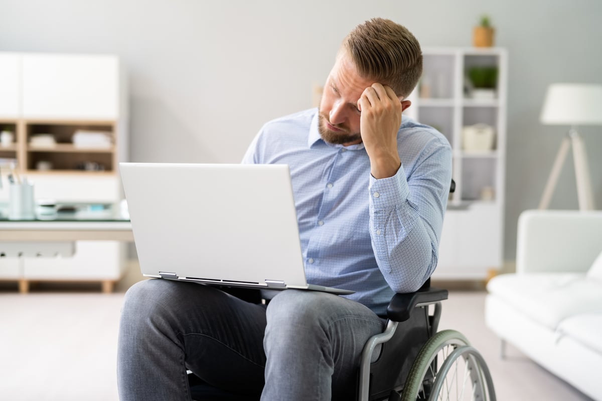 Person in wheelchair looking unhappy while wielding a laptop.