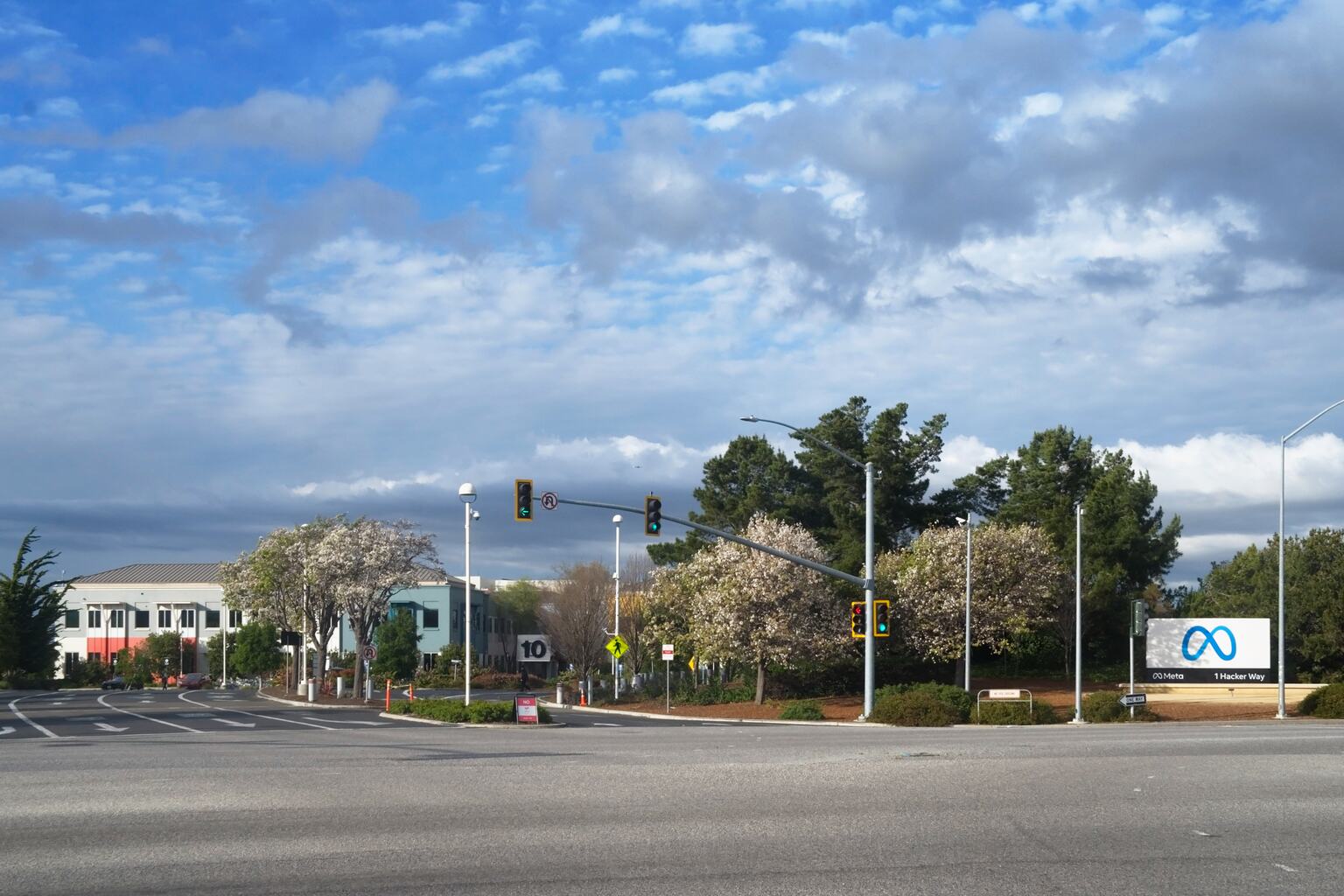 Documentary photograph of the entrance to Meta Platforms' headquarters complex at 1 Hacker Way in Menlo Park, California, showing the campus, roadway and Meta sign.